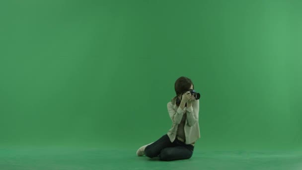 Sitzende junge Frau macht Fotos um sie herum auf dem grünen Bildschirm — Stockvideo