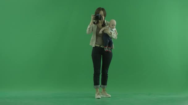 Una joven con su hijo tomando fotos a su alrededor en la pantalla verde — Vídeos de Stock