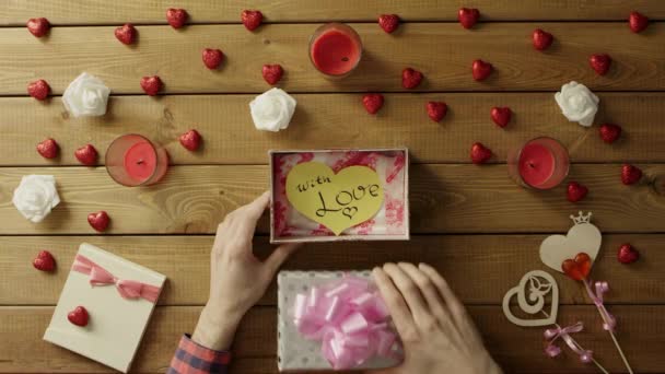 Молодой человек получает бумажное валентинное сердце ручной работы в подарок ко дню Святого Валентина, вид сверху — стоковое видео
