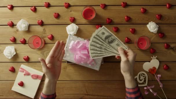 Человек кладет наличные деньги в подарочную коробку в качестве подарка для своего любимого, вид сверху — стоковое видео