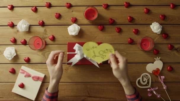 Молодий чоловік кладе серце валентинки на подарункову коробку, вид зверху — стокове відео