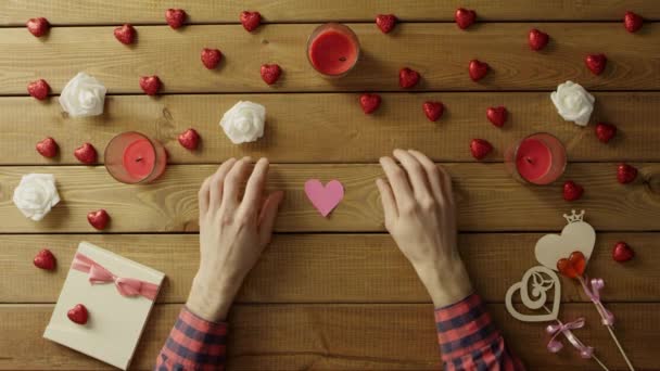 Jonge man met handgemaakte harten van papier zit door tabel, bovenaanzicht — Stockvideo
