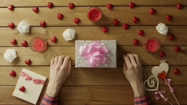 Молодий чоловік кладе валентинку на подарункову коробку, вид зверху — стокове відео