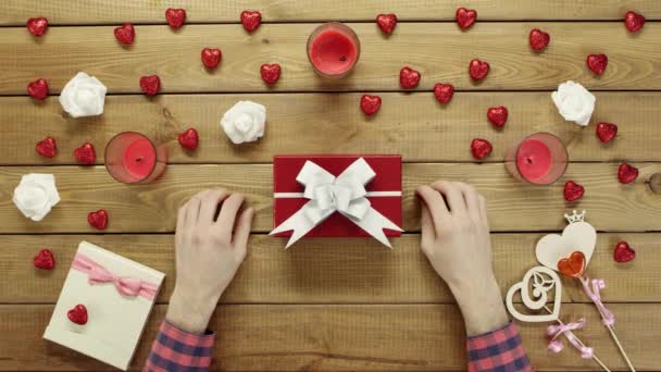 Man puts valentine onto present box for his wife, top view — Stock Video