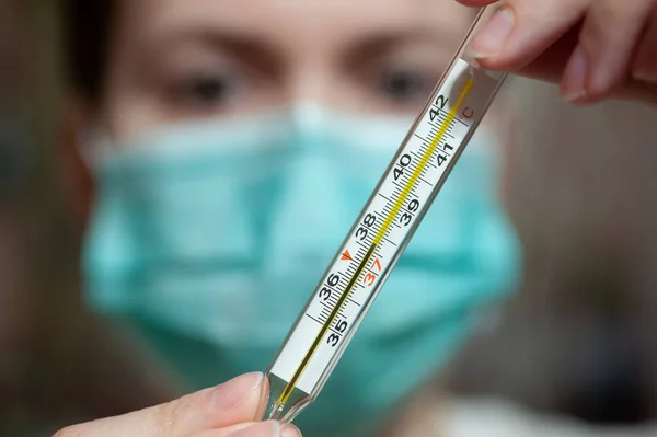 Doctor in facemask show a thermometer.