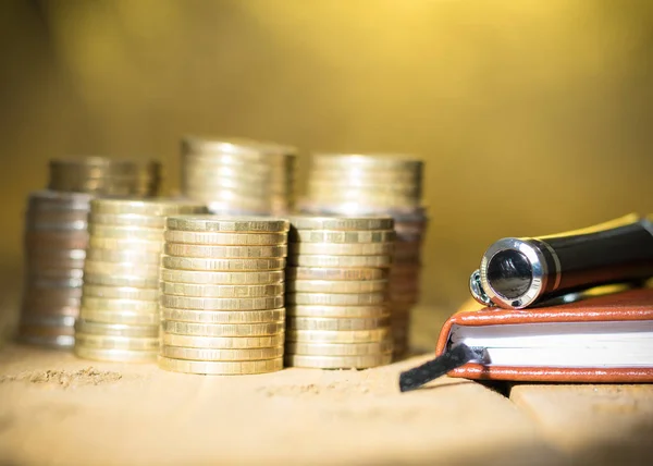 Monedas de metal con un cuaderno y una pluma estilográfica sobre una mesa rústica . — Foto de Stock