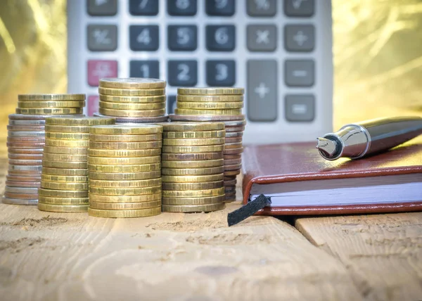 Pluma estilográfica, calculadora, monedas y cuaderno sobre una mesa de madera . — Foto de Stock