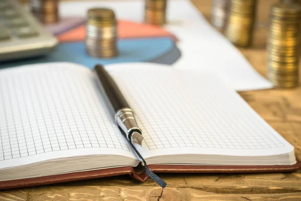 Pluma estilográfica, calculadora, monedas y cuaderno sobre una mesa de madera . — Foto de Stock