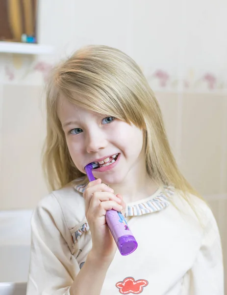 Une petite fille se brosse les dents avec une brosse à dents électrique . — Photo
