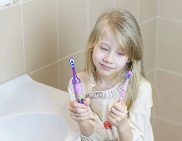 Kız elektrik ve geleneksel diş fırçaları karşılaştırır.