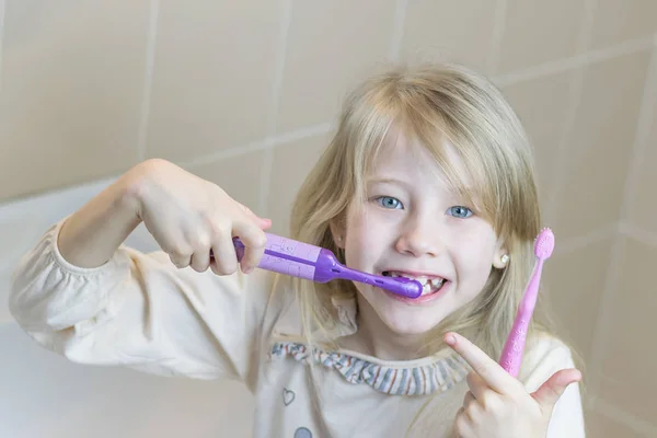 Kız iki farklı diş fırçası ile Dişlerini fırçalıyor.