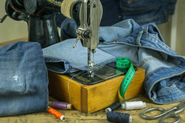 Vintage dikiş makinesi ile ahşap bir masa üzerinde denim. Giyim tamiri ve ev üretim kavramı.