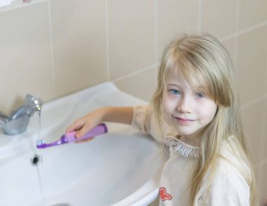 Kız bir banyoda elektrikli diş fırçası yıkar.