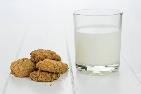 Un vaso de leche y galletas caseras sobre una mesa de madera blanca . — Foto de Stock