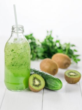 Taze salatalık, kivi ve salatalık güler yüzlü şişe beyaz ahşap masa üzerinde.