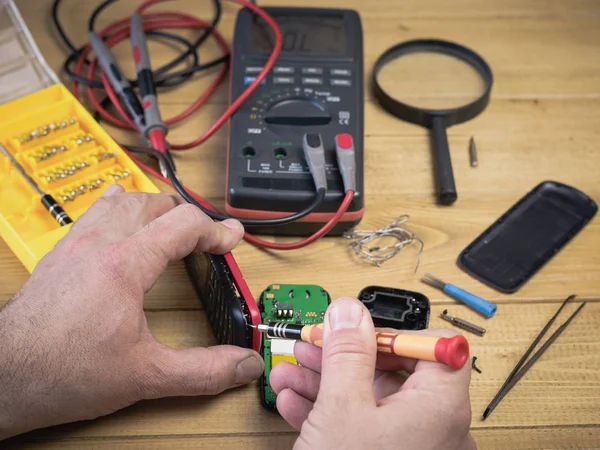 Een man onderzoekt een mobiele telefoon voor reparatie. — Stockfoto