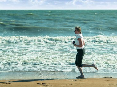 Kadın kulaklık ile sahilde koşu.