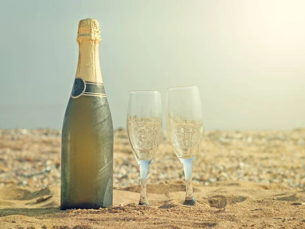 Dois copos e uma garrafa de champanhe em uma praia de areia em um dia quente de verão . — Fotografia de Stock