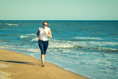 Çıplak ayak ile gözlüklü kadın sahilde koşu.