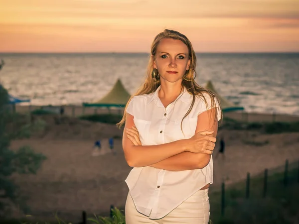 Retrato de una hermosa mujer con una camisa blanca sin mangas en el fondo del mar puesta del sol . — Foto de Stock