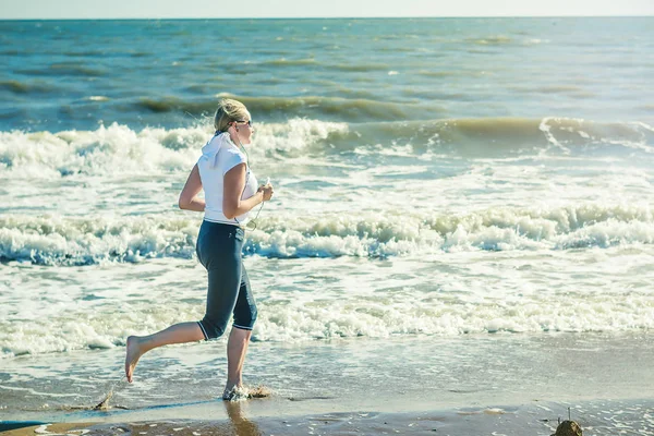 Bir kadın sabahın erken saatlerinde yükselen güneş ışınlarının içinde plaj boyunca çalışır.