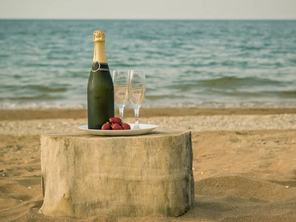Mesa de um pedaço de madeira com uma garrafa de champanhe e morangos junto ao mar . — Fotografia de Stock