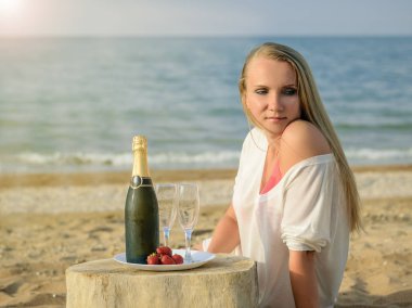 Parlak güneş ışığı ile bir şişe şampanya ve çilek sahilde güzel kadın.