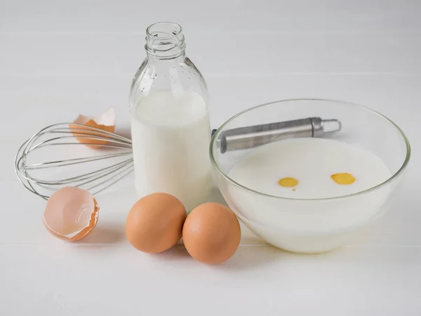 Cuenco con la mezcla de leche y huevo y huevos frescos en una mesa de madera blanca . — Foto de Stock
