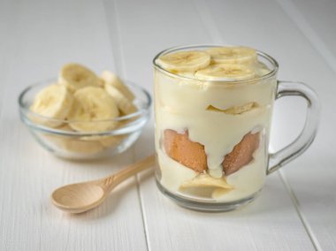 Bir cam kupa ve hafif ahşap masanın üzerine küçük bir kaşığı muz puding.