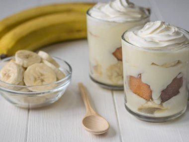 İki cam bardağı muz puding ile ahşap bir masa üzerine krem şanti ile tanımlama.
