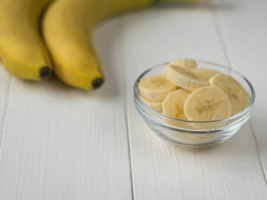 İki bütün muz ve muz dilimleri beyaz bir tabloda bir kase.