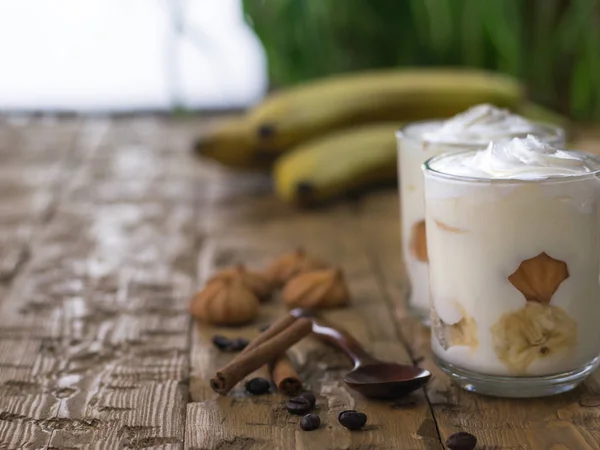 Makanan penutup pisang dengan coklat, krim, biskuit dan kayu manis di atas meja putih . — Stok Foto