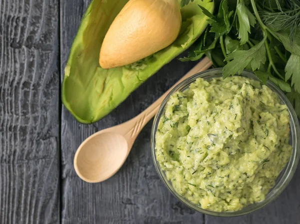 Küçük bir tahta kaşık, yeşillik bir avuç ve avokado ahşap bir masaya krem bir kase.