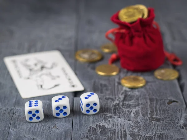 Münzen aus einer Tüte und rote Würfel auf einem dunklen Holztisch. — Stockfoto