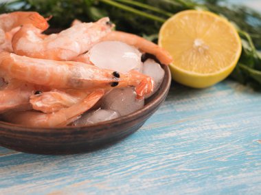 Limon ve maydanoz ahşap bir masa üzerinde bir toprak kapta karidesleri dondurulmuş.