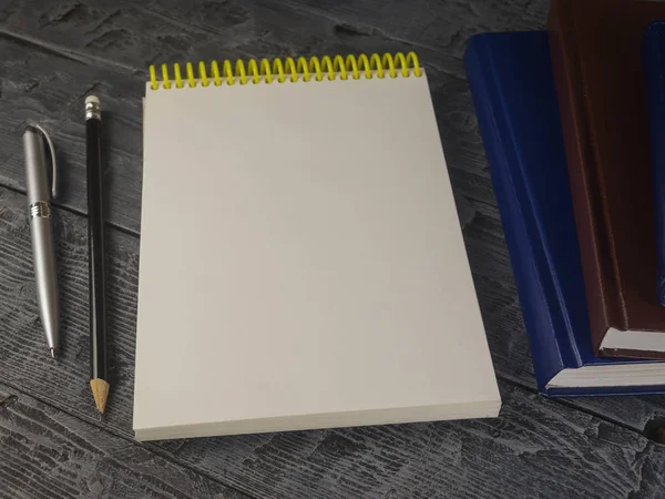 Open Kladblok, pen, potlood en boek op een houten tafel. — Stockfoto