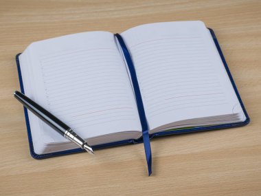 Siyah dolmakalem Not ile sarı ahşap Desk içindeki mavi ciltli kitap.