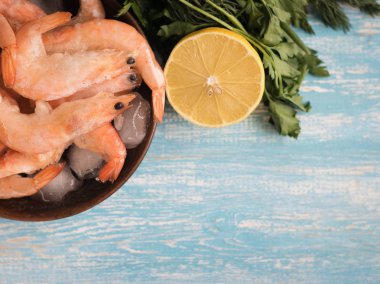 Limon ve maydanoz mavi ahşap bir masa üzerinde bir toprak beyaz kase dondurulmuş karides.