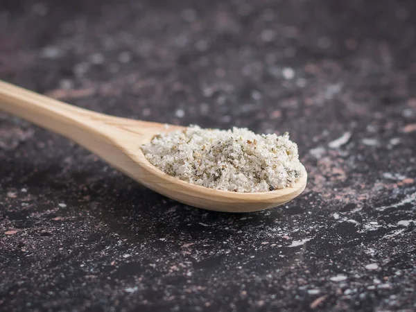 Pequeña cuchara marrón en una pila de sal con hierbas en la mesa de piedra oscura . — Foto de Stock