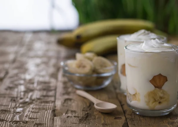 Banana dessert dengan whipped cream dan biskuit di atas meja kayu gelap pedesaan . — Stok Foto