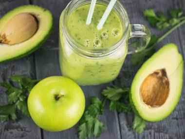 Taze avokado otlar ve iki kokteyl kamış ile smoothies siyah ahşap bir masa üzerinde yapılmış. Diyet vejetaryen yemek.