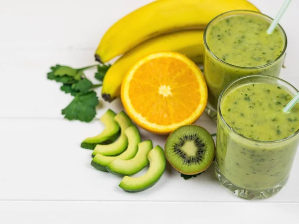 En nygjord smoothie med avokado, banan, persilja, citron, apelsin och kiwi på en vit träbord. Kost vegetarianmat. Råa livsmedel. — Stockfoto