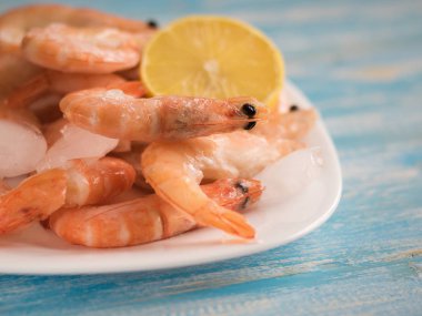 Beyaz dondurulmuş karides ve mavi ahşap bir masa üzerinde limon ile yemek.