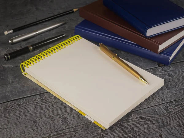 Open Kladblok, pen, potlood en boek over een zwarte houten tafel. — Stockfoto