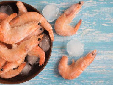 Buz parçaları ile iki dondurulmuş karides karides mavi bir tabloda bir kâse yakınındaki.