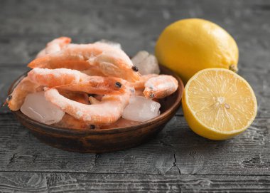 Limon ve otlar üzerinde siyah ahşap rustik masa kil kahverengi kase dondurulmuş karides.