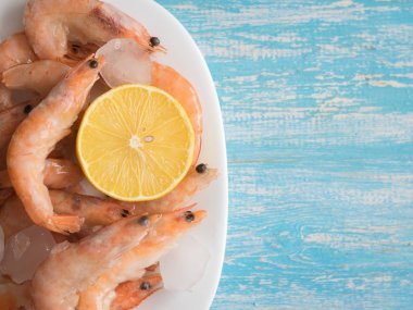 Limon ahşap bir masa üzerinde bir toprak beyaz kase dondurulmuş karides.