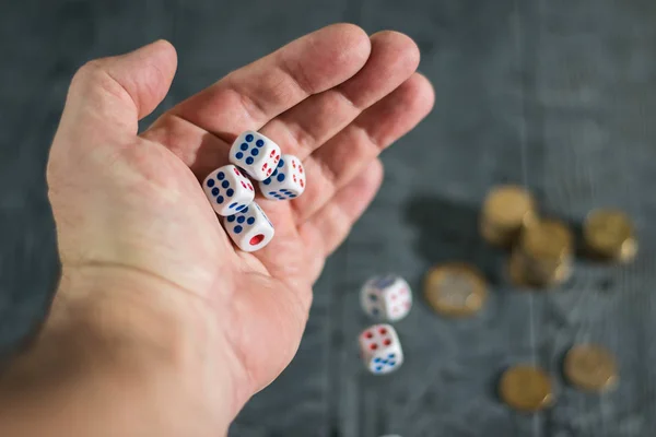 Würfel fallen aus der Hand eines Mannes auf einem schwarzen Holztisch mit goldenen Münzen. — Stockfoto