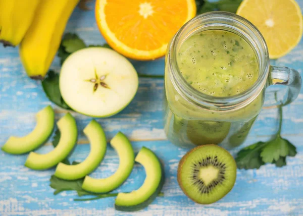 Avokado smoothie med kiwi, apelsin och banan och halvorna av en kiwi på blå träbord. Kost vegetarianmat. Råa livsmedel. — Stockfoto