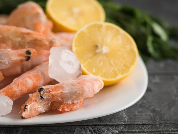 Koyu ahşap bir masa üzerinde bir kil kase dondurulmuş karides üzerinden buz parçaları.